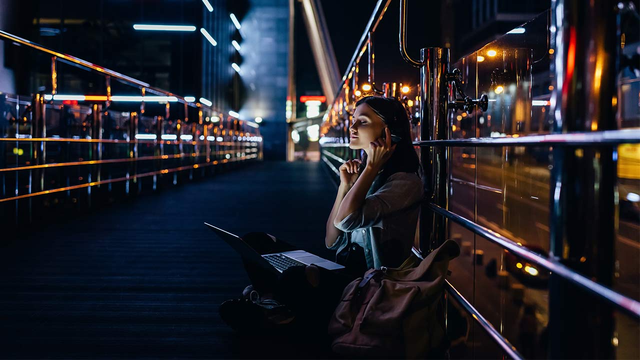 Foto de uma mulher sentada na rua com iluminação urbana.