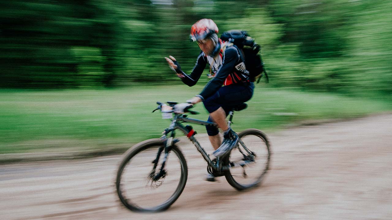 Homem andando de bicicleta na floresta, fotografado usando a técnica de Panning.