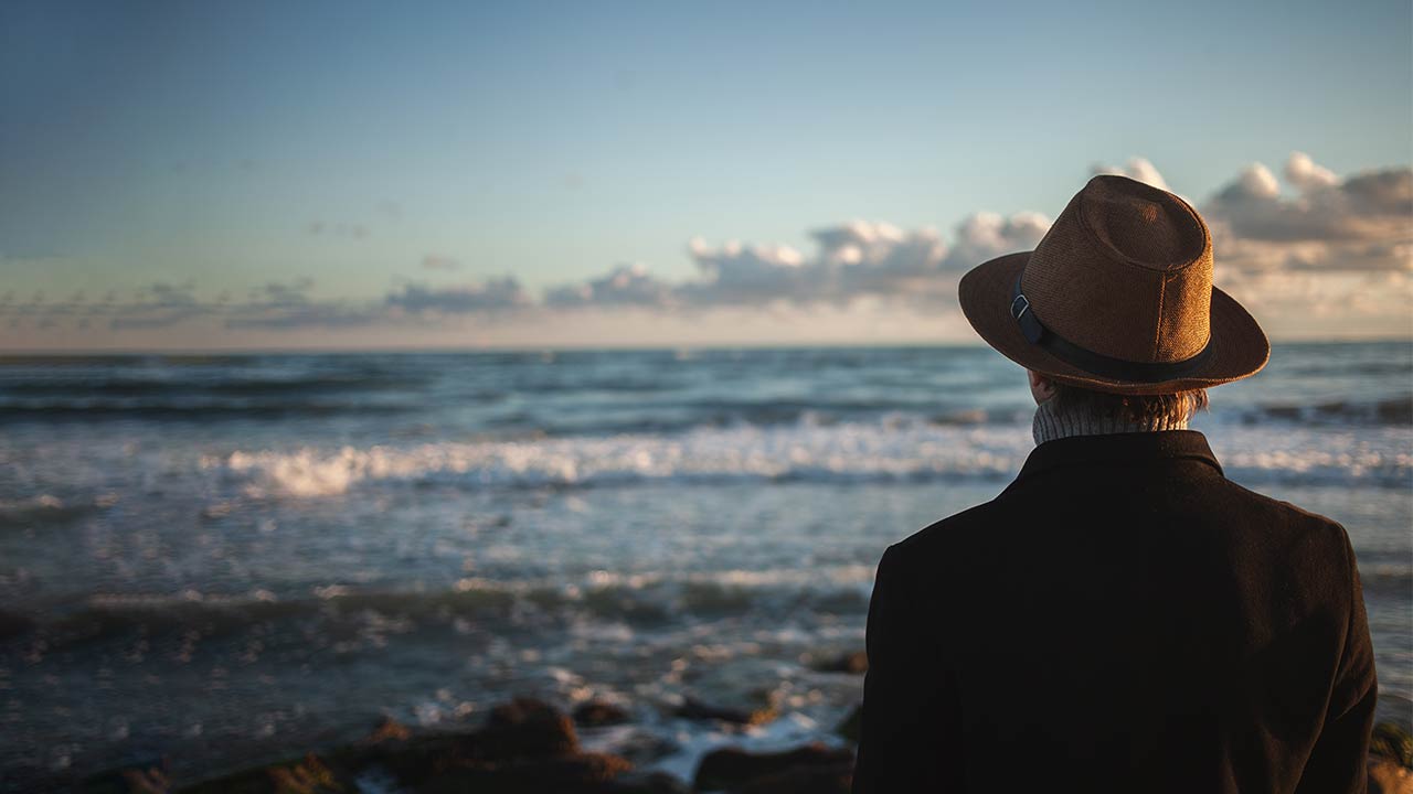 Homem de costas olhando para o oceano.