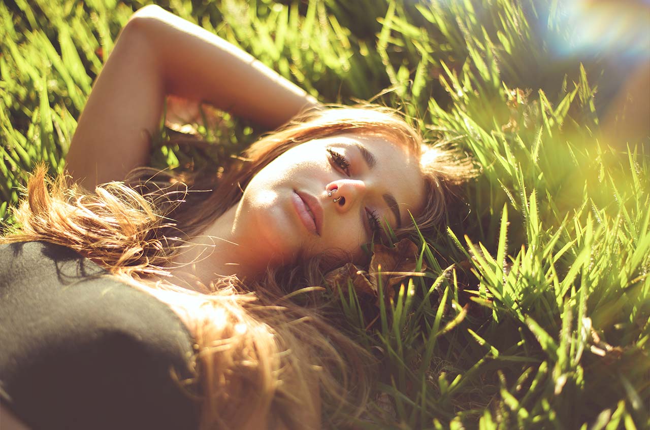 Menina fotografada em bosque, deitada sobre a grama, luz do dia.
